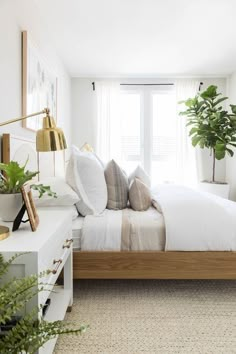 a bed with white sheets and pillows in a bedroom next to a plant filled window