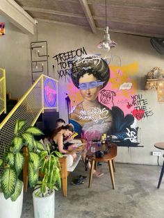 a woman sitting on a chair in front of a wall covered with graffiti and potted plants