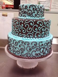 a three layer cake with blue icing and swirl designs on it's sides