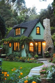 a green house with lots of windows and flowers around it's front door, surrounded by greenery