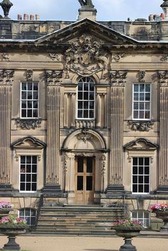 an old building with many windows and steps leading up to the front door that has flowers in large planters on each side