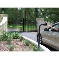 a woman standing next to a car in front of a gated area with trees