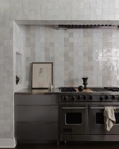 a stove top oven sitting inside of a kitchen next to a wall covered in white tiles