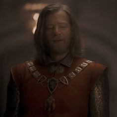 a man with long hair wearing a red and gold outfit in a dimly lit room