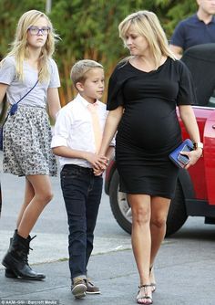 the pregnant woman is walking down the street with her husband and son, who are holding hands