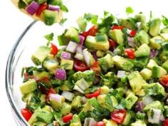 a bowl filled with chopped vegetables and dressing being spooned into the salad in it