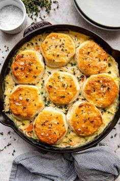 a casserole dish filled with baked biscuits and herbs on a white countertop