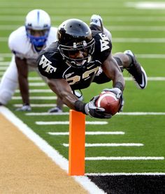 a football player dives over an orange pole to catch the ball during a game