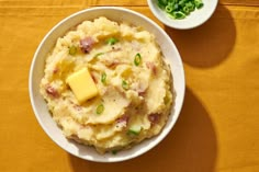 a bowl filled with mashed potatoes topped with cheese and scallions next to a small bowl of green peas