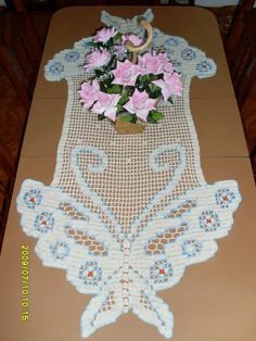 a table runner with pink flowers in a vase on top of it and an embroidered doily