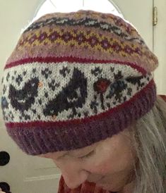 a woman is wearing a knitted hat and eating a donut while looking down at her cell phone