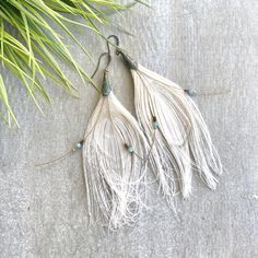 two pairs of earrings with white feathers and turquoise beads hanging from hooks on a gray surface