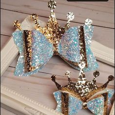 there are three little crowns on the table in front of a white photo frame with blue and gold sequins