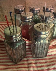 several jars with spoons in them sitting on a striped table cloth next to each other