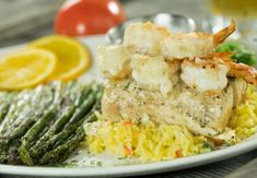 a white plate topped with shrimp, rice and asparagus next to lemon wedges