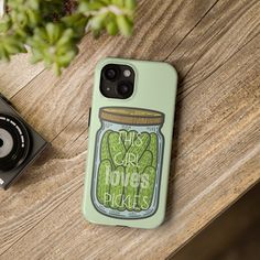 an iphone case with the words pickles on it next to a camera and plant