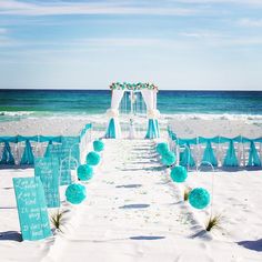 a beach wedding set up with blue and white decorations on the sand near the ocean