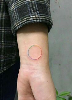 a person's hand with a small tattoo on their left wrist that has a rainbow circle in the middle