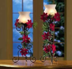 two candles are decorated with poinsettis and greenery on a table in front of a window