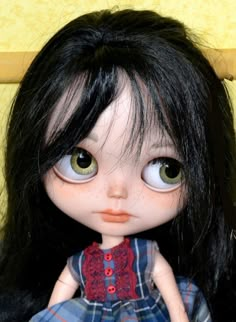 a close up of a doll with long black hair and green eyes wearing a dress