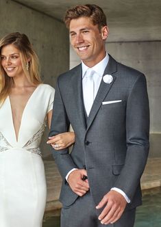 a man and woman standing next to each other in front of a fountain wearing formal attire