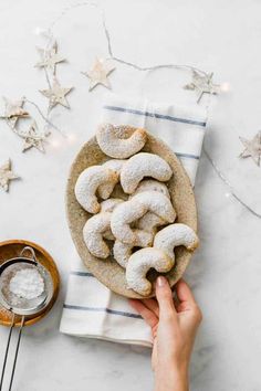 a person holding a plate with powdered donuts on it next to a bowl of sugar