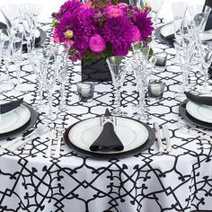 the table is set with black and white plates, silverware, and purple flowers