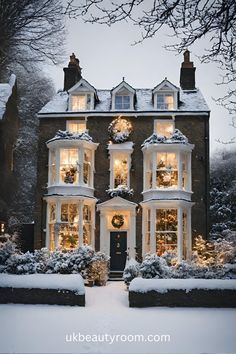 a large house covered in snow with christmas lights on it's windows and wreaths