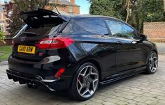 the back end of a black car parked on a brick road