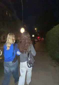 two women walking down the street at night with their backpacks on and one holding onto her back