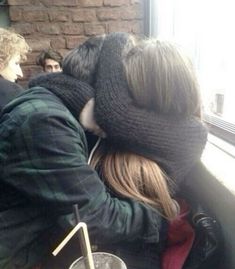 two people sitting next to each other in front of a window with their faces covered by mittens