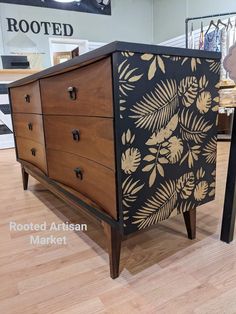 a black and gold painted chest of drawers on display in a room with wood floors