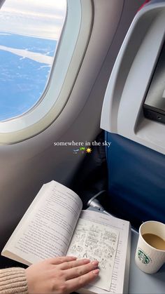 someone is reading a book and drinking coffee on an airplane with the view out the window