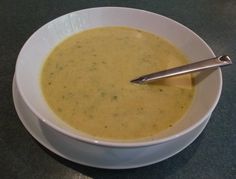 a white bowl filled with soup on top of a black counter next to a silver spoon