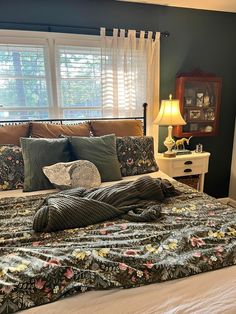 a bed with pillows and blankets on it in front of a window covered by curtains