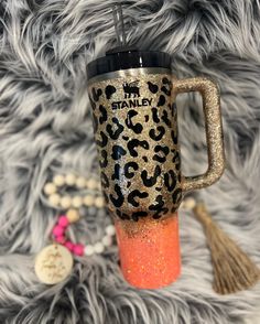 a leopard print travel mug with tassels and a keychain on a furry surface