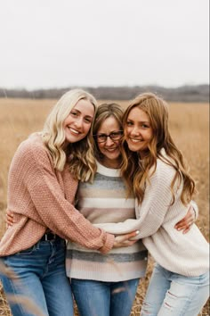 three beautiful women standing together in a field smiling at the camera with their arms around each other