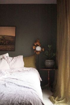 a bed with white linens and pillows in a dark room next to a painting on the wall