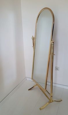 a gold standing mirror in the corner of a room with white walls and flooring