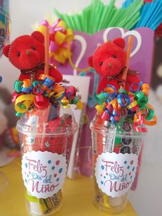 two red teddy bears sitting on top of cups filled with candy