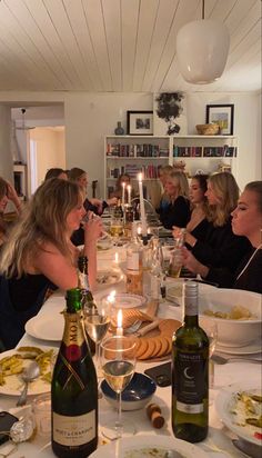 a group of women sitting around a dinner table with food and wine in front of them