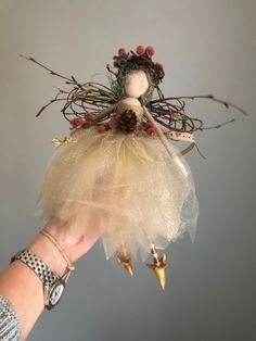 a hand holding a small doll with birds on it's wings and a pine cone