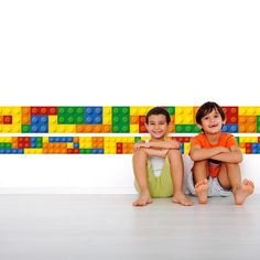 two young boys sitting on the floor in front of a wall with lego blocks behind them