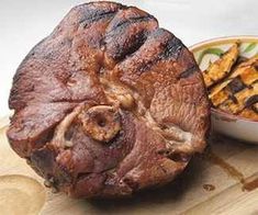 a large piece of meat sitting on top of a wooden cutting board next to a bowl of fries