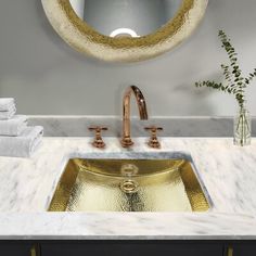 a bathroom sink under a round mirror with gold faucet and marble counter top