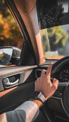 a man driving a car with his hand on the steering wheel and pointing to the left