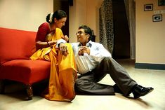 a man sitting on the floor next to a woman in a yellow sari and black shoes