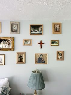 a wall with many framed pictures on it and a lamp next to the bed in front