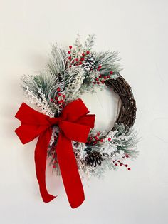 a christmas wreath with red ribbon and pine cones on the front, against a white background