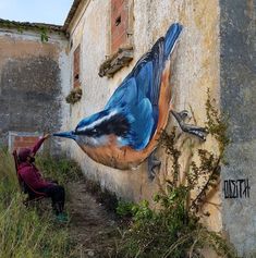 a blue bird painted on the side of a building next to a man kneeling down